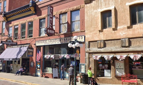 Historic saloon building with a sign, balloons, and people outside, featuring American flags and a lively atmosphere.