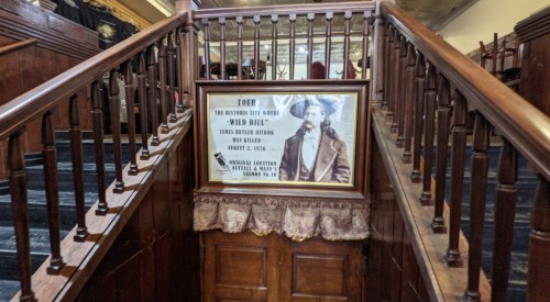 A wooden staircase leads to a framed poster about Wild Bill Hickok, detailing his history and significance.