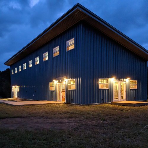 A modern blue metal building illuminated at dusk, featuring multiple windows and doors.