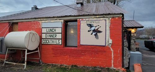 A red brick building with signs for lunch, dinner, and cocktails, featuring a mural of birds on the wall.