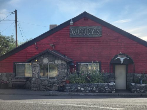 A rustic building with a sign reading "Woody's," featuring a stone facade and a welcoming entrance.