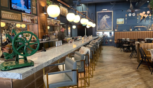 A stylish bar with a marble countertop, modern seating, and a bear painting on the wall, featuring a well-stocked bar.