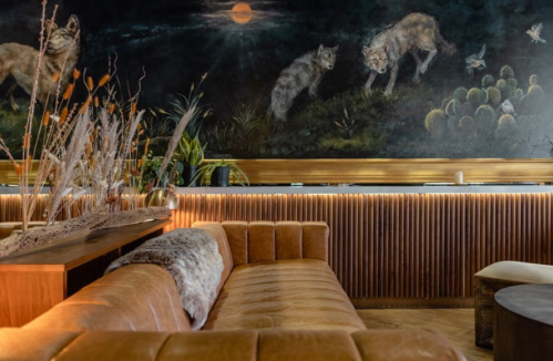Cozy restaurant interior featuring a leather sofa, wooden accents, and a mural of wolves and nature.