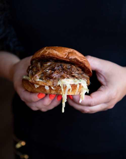 A person holding a juicy burger with caramelized onions and melted cheese, served on a soft bun.
