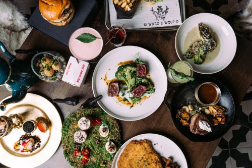 A variety of dishes including salads, burgers, desserts, and drinks arranged on a wooden table.