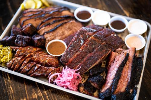 A platter of assorted smoked meats, including brisket, sausage, and ribs, served with various sauces and pickles.