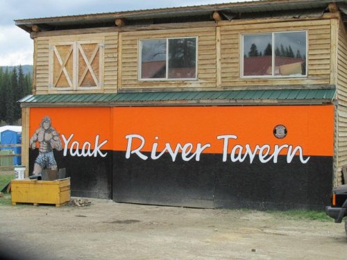 Exterior of the Yaak River Tavern, featuring a wooden building with an orange and black mural and a statue outside.