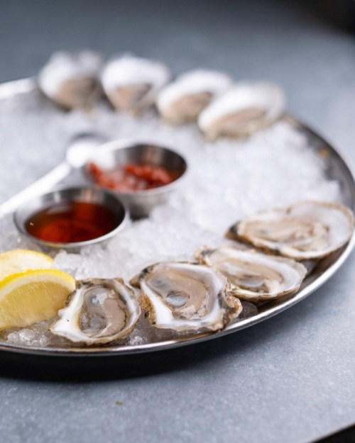 A platter of fresh oysters on ice, served with lemon wedges and dipping sauces.