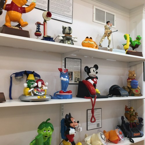 Colorful vintage toys and novelty phones displayed on white shelves, featuring characters like Mickey Mouse and Winnie the Pooh.
