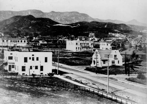 Historic black-and-white photo of a small town with buildings and mountains in the background.