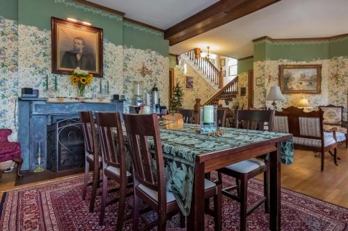 A cozy dining area with a wooden table, floral wallpaper, a fireplace, and a staircase in the background.