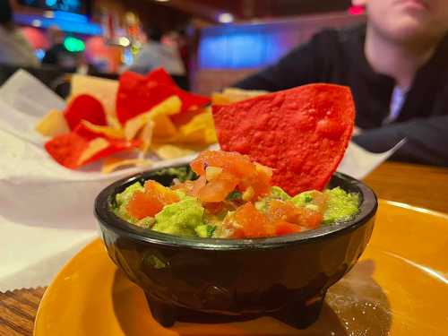 A bowl of guacamole topped with diced tomatoes, served with red and yellow tortilla chips on a plate.