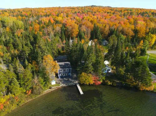 Aerial view of a lakeside house surrounded by vibrant autumn foliage and trees.