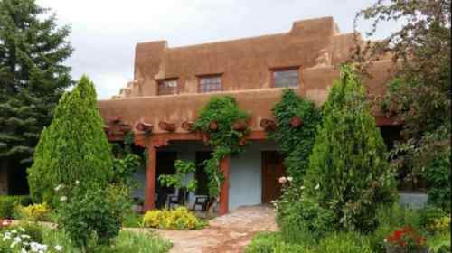 A charming adobe-style house surrounded by lush greenery and colorful flowers under a cloudy sky.