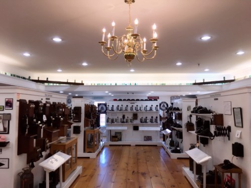 A well-lit museum room displaying various vintage cameras and photography equipment on white shelves.