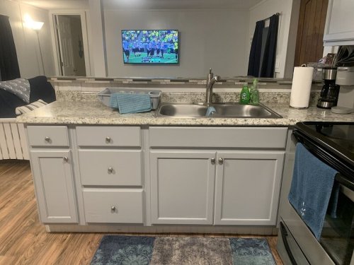 A kitchen with a granite countertop, sink, and cabinets, featuring a TV in the background showing a sports game.