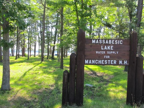 Sign for Massabesic Lake, indicating it's a water supply for Manchester, NH, surrounded by trees and greenery.