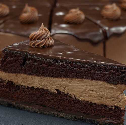 A slice of rich chocolate cake with creamy chocolate filling and a decorative swirl on top.