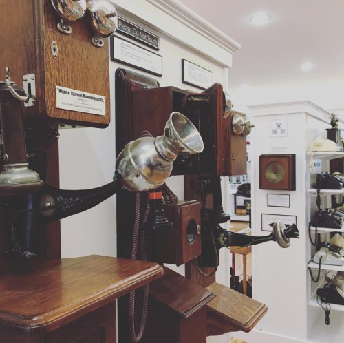 A display of vintage wooden telephones with metal components in a museum setting.