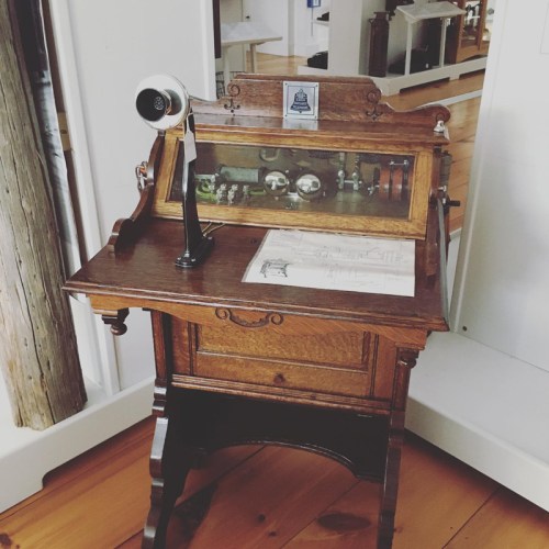 A vintage wooden desk with a glass display, featuring a telephone and historical documents.