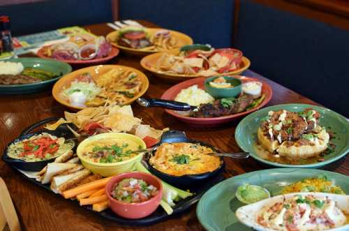 A variety of colorful dishes including nachos, tacos, and grilled meats served on plates and platters.