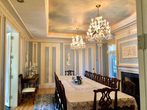 Elegant dining room with a long table, ornate chandeliers, and decorative wall panels in soft colors.