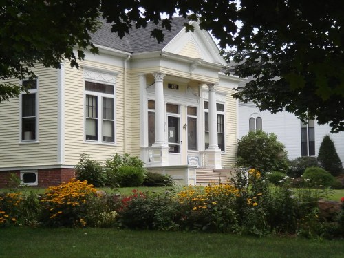 A charming yellow house with white columns, surrounded by colorful flowers and greenery.