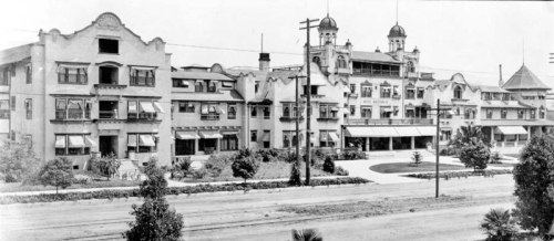 Historic black-and-white photo of a large, ornate building with balconies and a landscaped front area.