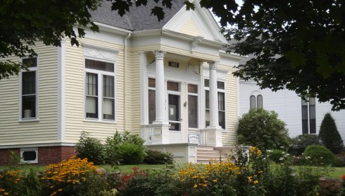 A charming yellow house with white columns, surrounded by colorful flowers and greenery.