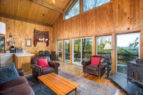 Cozy wooden living room with large windows, a fireplace, and a view of nature. Comfortable seating and a coffee table.