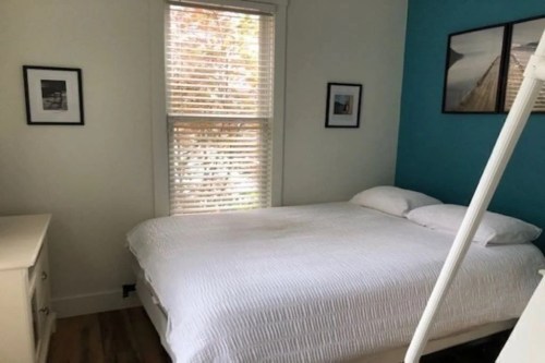 A cozy bedroom featuring a white bed, blue accent wall, and framed pictures near a window with blinds.