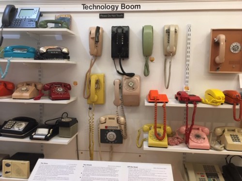 A display of vintage telephones in various colors and styles, labeled "Technology Boom," with a sign saying "Please Do Not Touch."