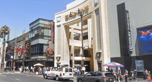 A busy street view featuring the Dolby Theatre and nearby shops, with people walking and vehicles parked.