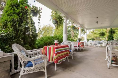 A cozy porch with striped tablecloths, wicker chairs, and hanging plants, surrounded by greenery.