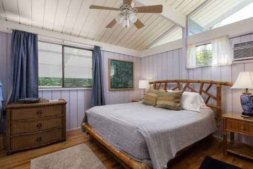 Cozy bedroom with a bamboo bed, light purple walls, and large windows, featuring a dresser and bedside lamps.