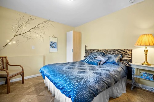 Cozy bedroom featuring a blue patterned bedspread, wooden headboard, lamp, and a decorative branch on the wall.