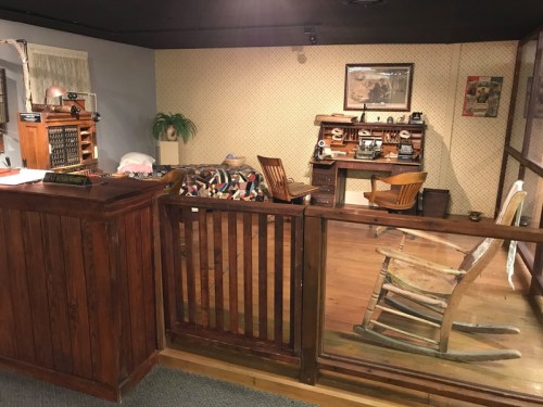 A vintage room with a wooden desk, rocking chair, and decorative items, resembling a historical setting.