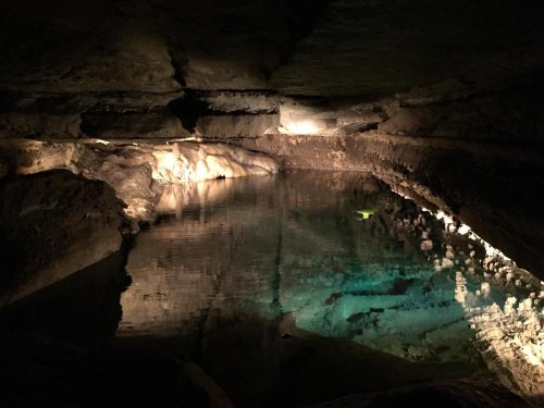 A dimly lit cave with a still water pool reflecting the rocky walls and soft lighting.