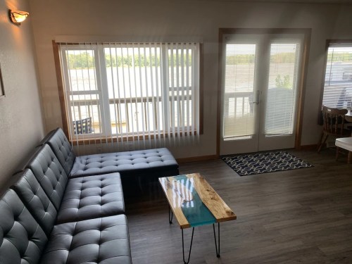 Cozy living area with a gray sectional sofa, wooden table, and large windows overlooking a scenic view.