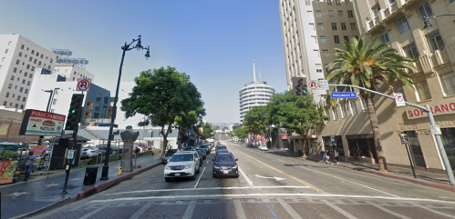 A busy street in Hollywood with palm trees, buildings, and cars under a clear blue sky.
