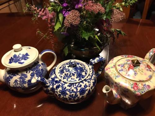 Three decorative teapots in blue and white patterns, alongside a floral-patterned teapot, with a bouquet in the background.