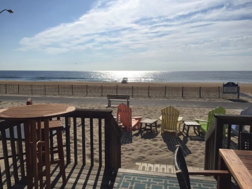 A serene beach view with colorful chairs, a wooden deck, and calm waves under a bright sky.
