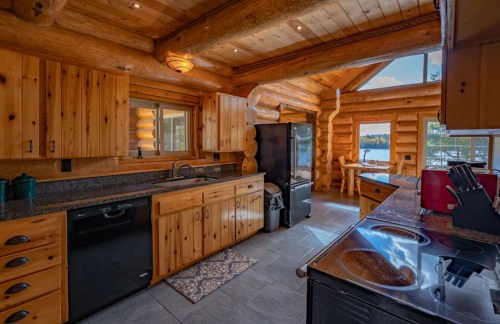 Cozy log cabin kitchen with wooden cabinets, modern appliances, and a view of the lake through large windows.