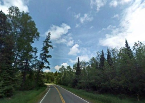 A winding road surrounded by lush green trees under a partly cloudy sky.