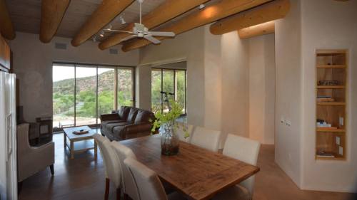 Modern interior featuring a dining table, leather sofa, and large windows with a view of nature. Warm, earthy tones.