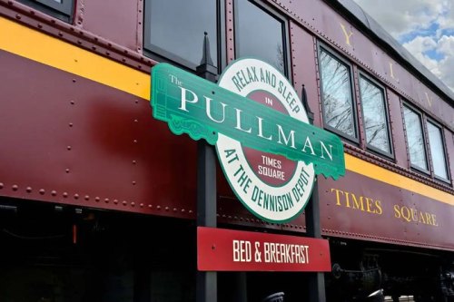Sign for The Pullman Bed & Breakfast at the Dennison Depot, featuring a vintage train car and a blue sky.