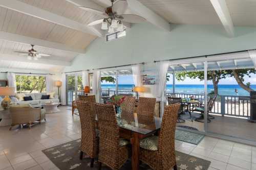 Bright coastal living space with large windows, dining table, and views of the ocean and beach outside.