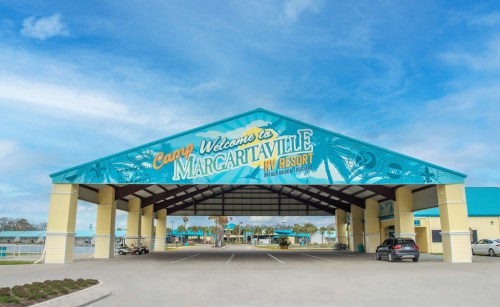 Entrance to Camp Margaritaville RV Resort, featuring a colorful sign and a spacious covered area under a blue sky.