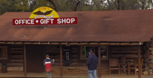A rustic gift shop with a sign reading "Welcome to Eagle Cave," featuring two people outside.