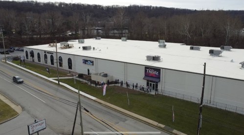 Aerial view of a large white building with a sign reading "Thrillz," and a line of people outside along the road.